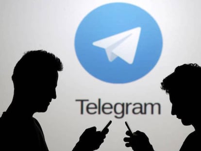 Dos hombres consultan sus teléfonos móviles delante del logotipo de la aplicación Telegram.
 