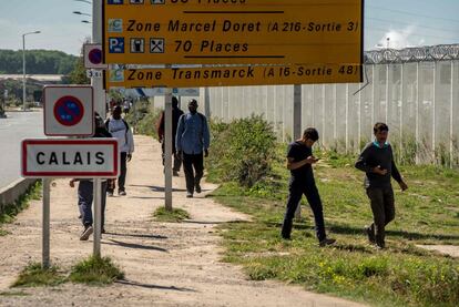 Migrantes caminan al lado del cartel de entrada a Calais, cerca del campo de refugiados conocido como 'La Jungla'. El Gobierno regional ha solicitado el cierre del campamento por la noche para que los migrantes no caminen por los alrededores.