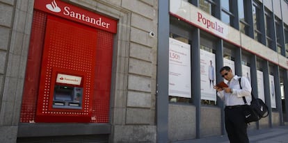 Un hombre espera junto a un cajero automático de Banco Santander.