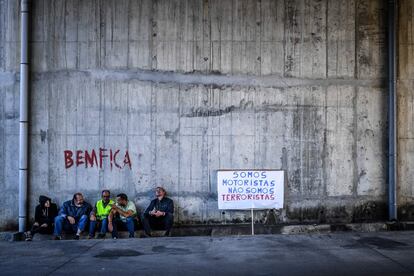 Manifestantes se sientan al lado de una pancarta que dice "Somos conductores, no terroristas", durante el primer día de una huelga de conductores de camiones cisterna en Aveiras de Cima (Portugal). En medio de lo que el gobierno ha denominado como una crisis energética, se ha decidido este lunes racionar la cantidad de combustible que pueden adquirir los ciudadanos. Los conductores podrán acceder a un máximo de 15 litros de gasolina o diésel por llenado en estaciones especialmente designadas y 25 litros en todas las demás estaciones.