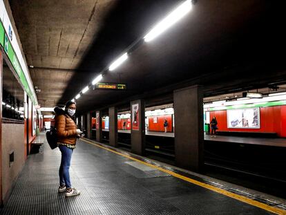 Una mujer protegida con una máscara espera en un solitario andén de una estación de metro, en Milán.