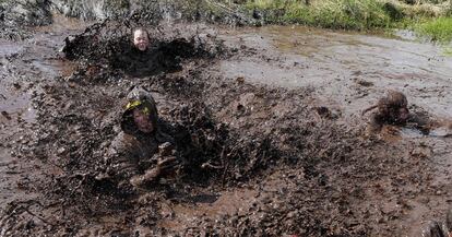 Tres participantes del desafio Mud Madness, celebrado en Portadownse, se revuelcan en el barro (Irlanda del Norte).