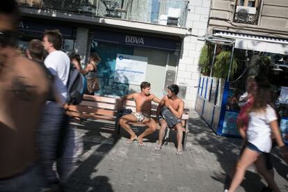 Dos turistas en ba&ntilde;ador descansan en un banco de la Barceloneta. 