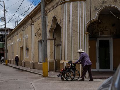 Un hombre empuja la silla de ruedas de su mujer frente a un hotel quemado por el narcotráfico en Aguililla, Estado de Michoacán, el 8 de julio de 2021.