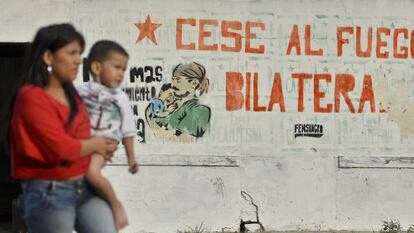 Una mujer pasa junto a su hijo ante un cartel sobre el proceso de paz en el departamento de Cauca, Colombia.