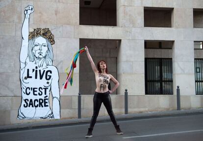 Una activista femenina con una inscripción pintada en su pecho, posa frente a una obra de arte con una inscripción que se traduce como "IVG (Ley sobre el aborto voluntario) es sagrado" en Marsella, Francia.