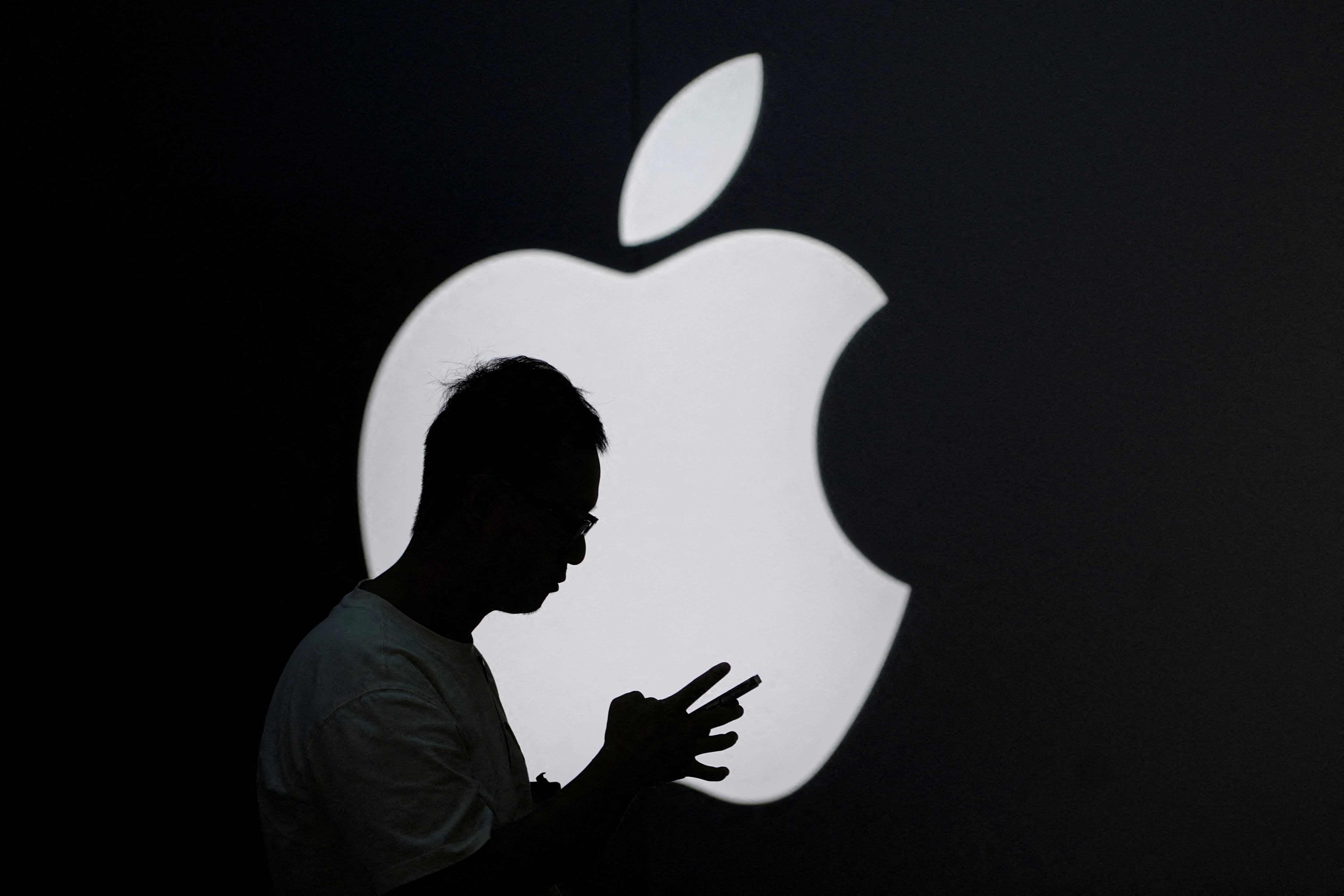 Un hombre mira su teléfono móvil cerca de un logotipo de Apple a la afuera de una tienda en Shanghái, China.