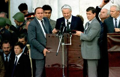 El líder de la era soviética, Boris Yeltsin (c), junto a su jefe de guardia Alexander Korzhakov (i) que sujeta un escudo a prueba de balas, mientras imparte un discurso, durante el funeral de las víctimas.