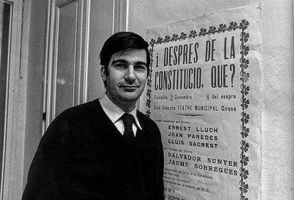 Ernest Lluch, ante un cartel que anuncia su participación en un debate en Girona.