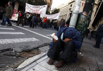 Un mendigo pide lismona al paso de una manifestaci&oacute;n contra los recortes en Atenas.