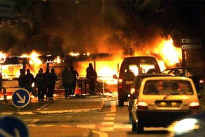 Un grupo de jóvenes de los suburbios contempla un autobús ardiendo en la localidad de Reynerie, cerca de Toulouse.