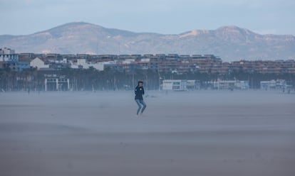 Una mujer camina por la playa mientras soplan fuertes rachas de viento, en Valencia.