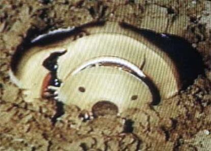 La cápsula, seriamente dañada y semienterrada en el desierto, en una imagen tomada de un vídeo de la NASA.