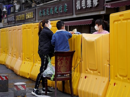 Una mujer paga la compra de un mercadillo delimitado por una barrera levantada durante la cuarentena, en Wuhan.
