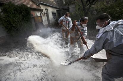 Miembros de los equipos de limpieza del vertido, protegidos con trajes especiales y mascarillas, echan yeso sobre el lodo contaminante para neutralizarlo en Devecser