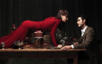 Una mujer encima de una mesa con comida mientras un hombre la mira.