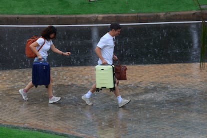 Dos personas con equipaje caminan bajo la lluvia en el aeropuerto de Manises (València) el 24 de julio de 2025.