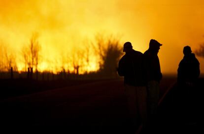 En la imagen, aparecen varias personas silueteadas contra el resplandor del fuego mientras observan un gran incendio de hierba ardiendo fuera de control, en el noreste de Hutchinson, Kansas (EE UU)