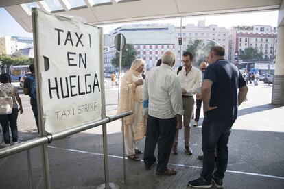 Viajeros conversan junto a un cartel de "Taxi en huega" en la estación de Atocha de Madrid.
