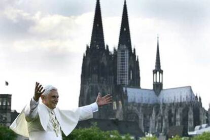 El papa Benedicto XVI saluda a los peregrinos mientras recorre el Rin en barco, con la catedral de Colonia al fondo.