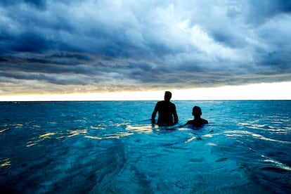 Two men take a dip in the ocean in Cuba, with storm clouds approaching.