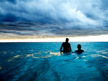 Two men take a dip in the ocean in Cuba, with storm clouds approaching.