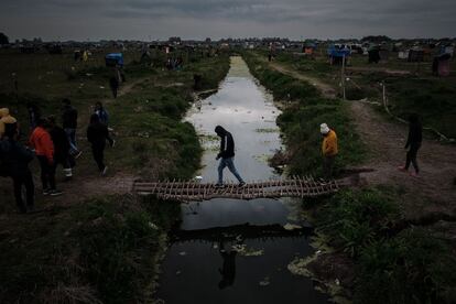 Varias personas cruzan un arroyo por un puente improvisado, en la localidad de Guernica, a 30 km de Buenos Aires (Argentina). Más de mil personas en situación de pobreza se instalaron desde el 20 de julio en un terreno de 100 hectáreas ubicado en dicha localidad.