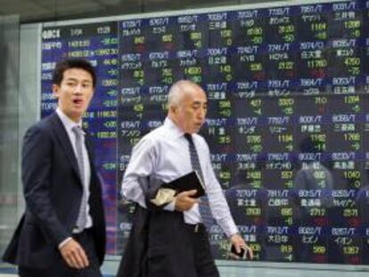 Dos viandantes pasan por delante de una pantalla con los resultados de la bolsa de Tokio (Japón). EFE/Archivo