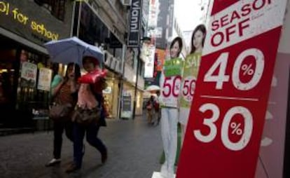 Dos mujeres surcoreanas pasan junto a un cartel que anuncia rebajas en una tienda de Seúl, Corea del Sur.