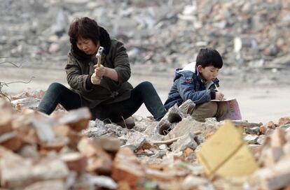 Un niño hace los deberes mientras su abuela trabaja buscando barras de acero reciclables entre los restos de un edificio demolido en Zhengzhou, China.