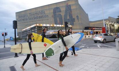 Unos surfistas pasan por delante del Kursaal, iluminado con el logo del Festival de Cine.