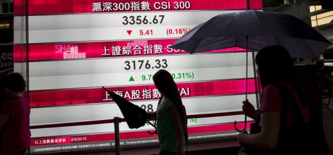 Unas personas pasan junto a un panel que muestra las cifras de los índices bursátiles de China y del Hang Seng, en el distrito financiero Central de Hong Kong, China.