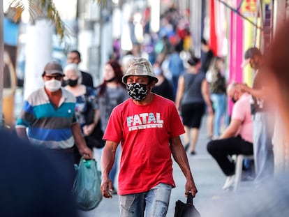 Pessoas com máscaras em frente a lojas fechadas devido à quarentena em São Paulo.