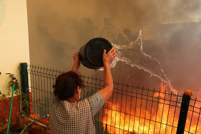 Una mujer tira agua para extinguir las llamas cerca de su casa en Vilarinho, Portugal, este martes.