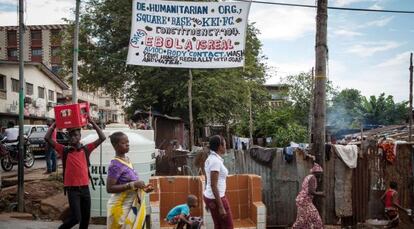 Varias personas pasan junto a un cartel de aviso contra el &eacute;bola en Freetown (Sierra Leona).
 