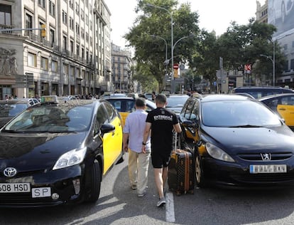Varios turistas pasan entre los taxis que ocupan la Gran Vía de Barcelona, durante la última huelga del sector.