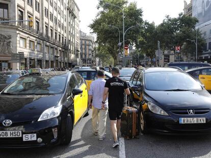 Varios turistas pasan entre los taxis que ocupan la Gran Vía de Barcelona, durante la última huelga del sector.