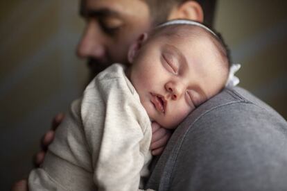 Un bebé duerme sobre el regazo de su padre. 