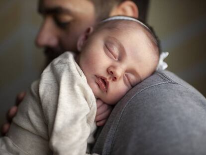 Un bebé duerme sobre el regazo de su padre. 