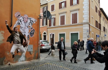 Un turista posa delante de una pintada, del artista italiano Mauro Pallotta que representa al papa Francisco como Superman, en una pared del barrio de Borgo Pio, cerca de la Plaza de San Pedro en Roma (Italia). 