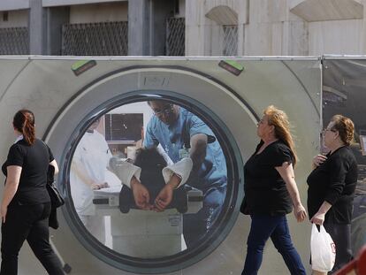 Dos mujeres pasean por delante de un cartel utilizado para cubrir obras en el hospital Virgen del Rocío.