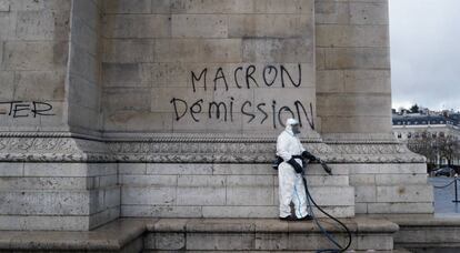 Un trabajador junto a una pintada contra el presidente Macron, este domingo en el Arco del Triunfo (París).