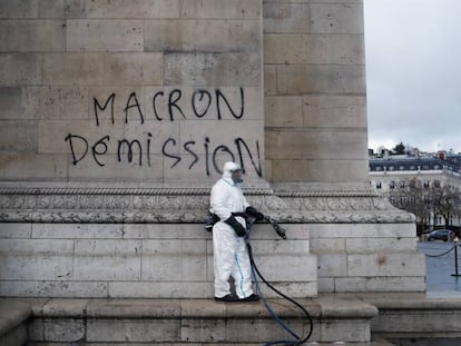 Un trabajador junto a una pintada contra el presidente Macron, este domingo en el Arco del Triunfo (París).