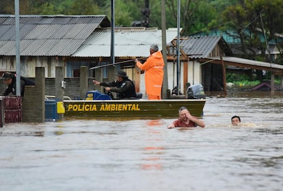 Police officers check a house as residents wade through a flooded street after floods caused by a cyclone in Passo Fundo, Rio Grande do Sul state, Brazil