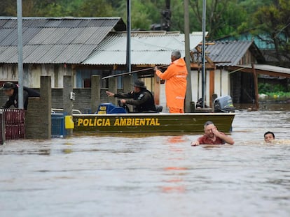 Police officers check a house as residents wade through a flooded street after floods caused by a cyclone in Passo Fundo, Rio Grande do Sul state, Brazil