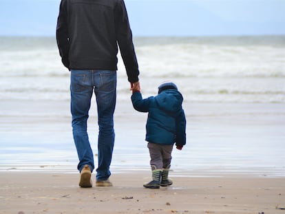 Un padre camina con su hijo por la playa.