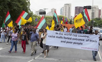 Manifestantes com bandeiras e um cartaz que diz "No país da Copa do Mundo, shoppings racistas proíbem a entrada de pessoas negras e pobres".