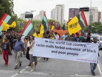 Manifestantes com bandeiras e um cartaz que diz "No país da Copa do Mundo, shoppings racistas proíbem a entrada de pessoas negras e pobres".