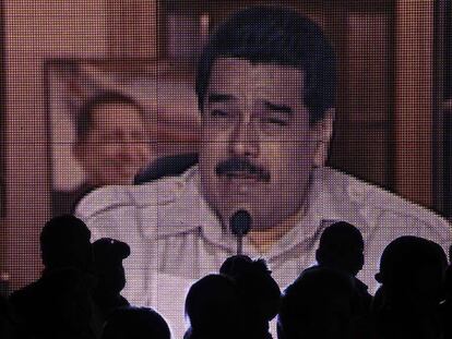 Varias personas miran una pantalla gigante donde se ve Nicolas Maduro en uno de sus programas televisivos.