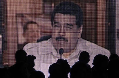 Varias personas miran una pantalla gigante donde se ve Nicolas Maduro en uno de sus programas televisivos.
